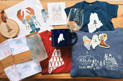 An assortment of Maine-inspired gifts including mugs, tea towels, prints, ornaments, glassware and apparel.
